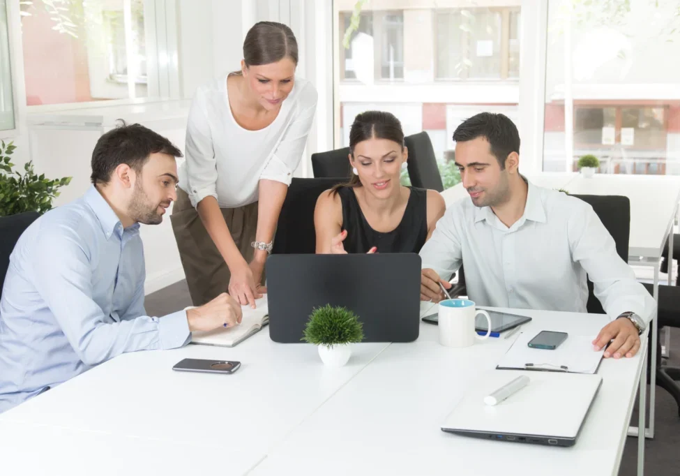 Group collaborating around a laptop in office.